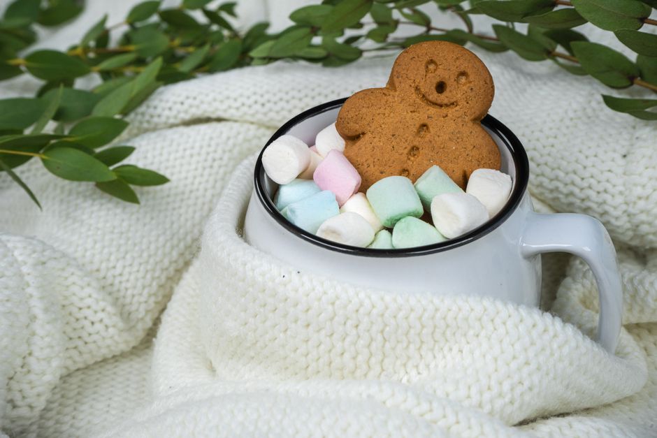 A cozy cup filled with marshmallows and a gingerbread cookie, wrapped in a white knit blan