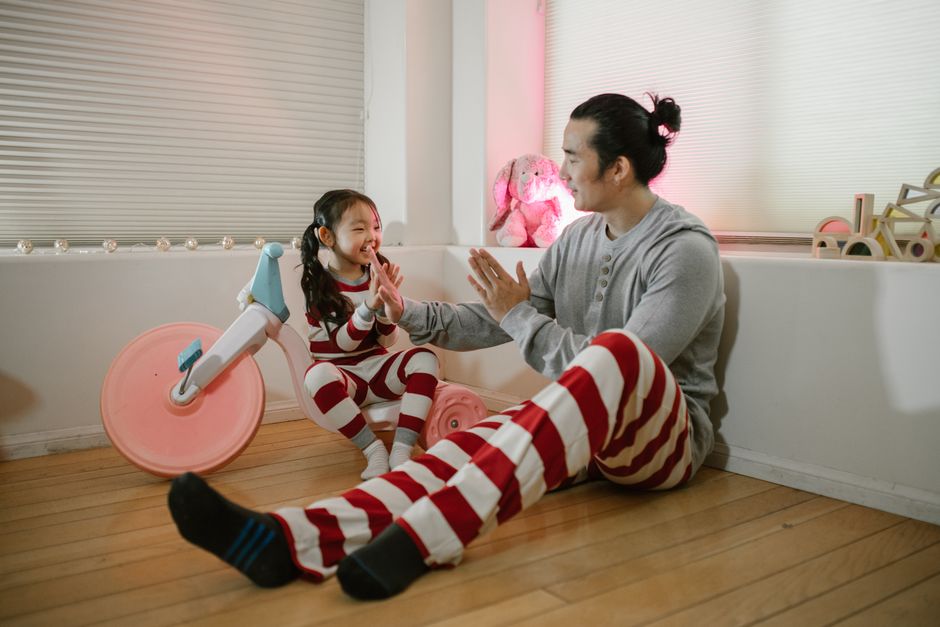 A father and daughter share a moment playing together indoors in matching pajamas.