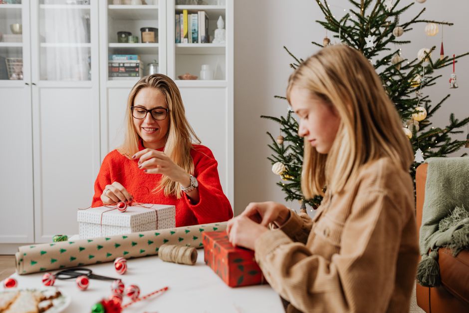 A mother and daughter wrapping Christmas gifts together at home, creating a warm holiday a