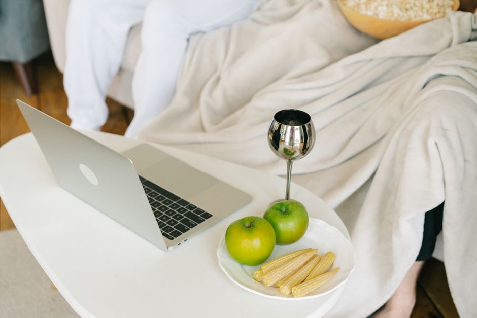 A relaxing indoor setup featuring a laptop, green apples, baby corns, and a decorative cup