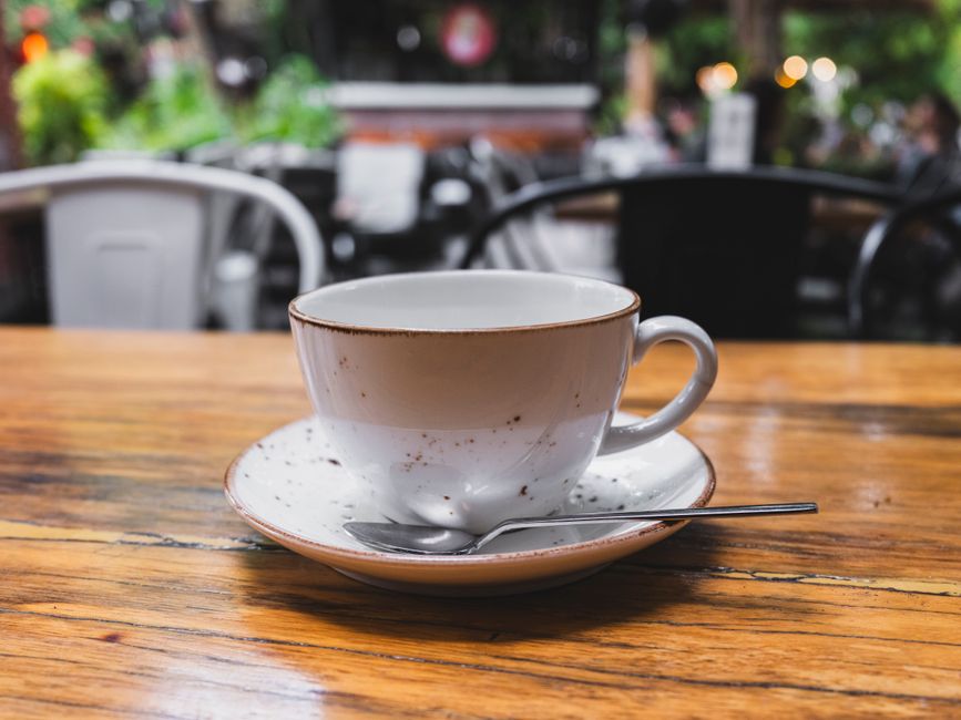 A rustic ceramic coffee cup with saucer on a wooden table in a café setting.