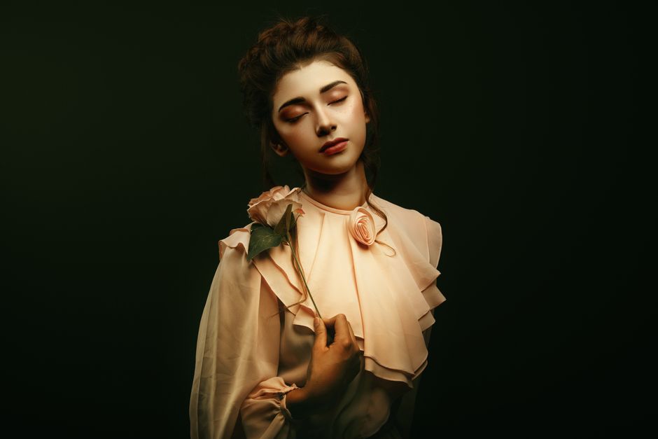 A serene portrait of a woman in elegant attire holding a rose, set against a green backgro