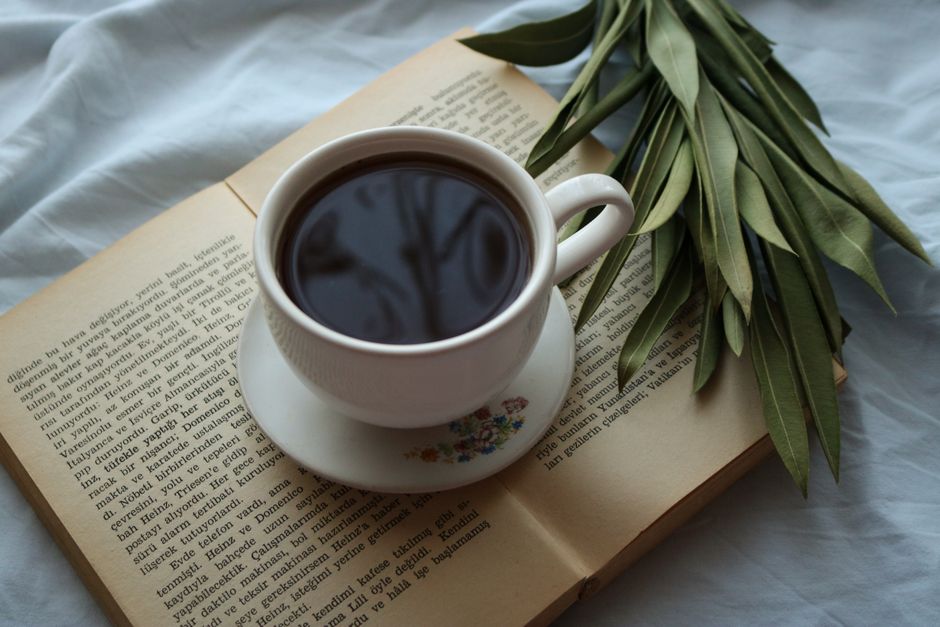 A serene setup with a cup of black coffee on an open book, accompanied by leaves.