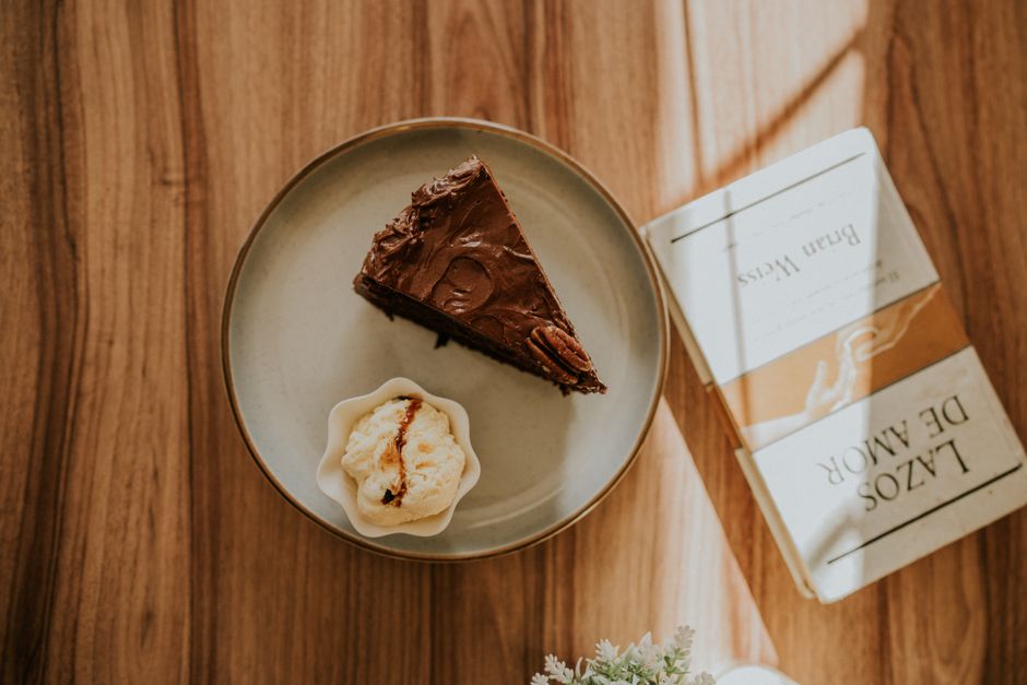 A top view of a chocolate cake slice, ice cream, and book on a wooden table, bathed in war