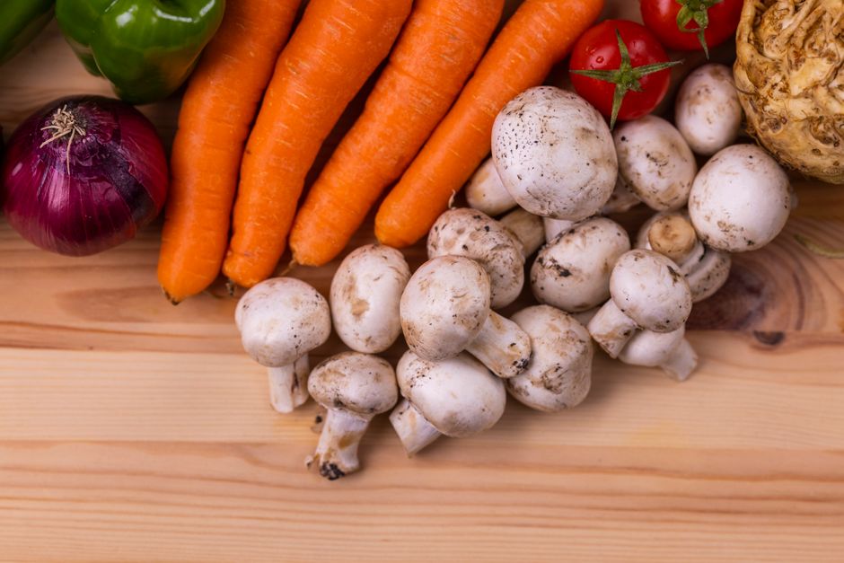 A variety of fresh organic vegetables including carrots, mushrooms, and tomatoes on a wood