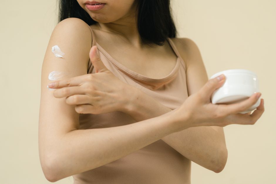 A woman applies moisturizing cream to her arm, focusing on skincare and self-care rituals 