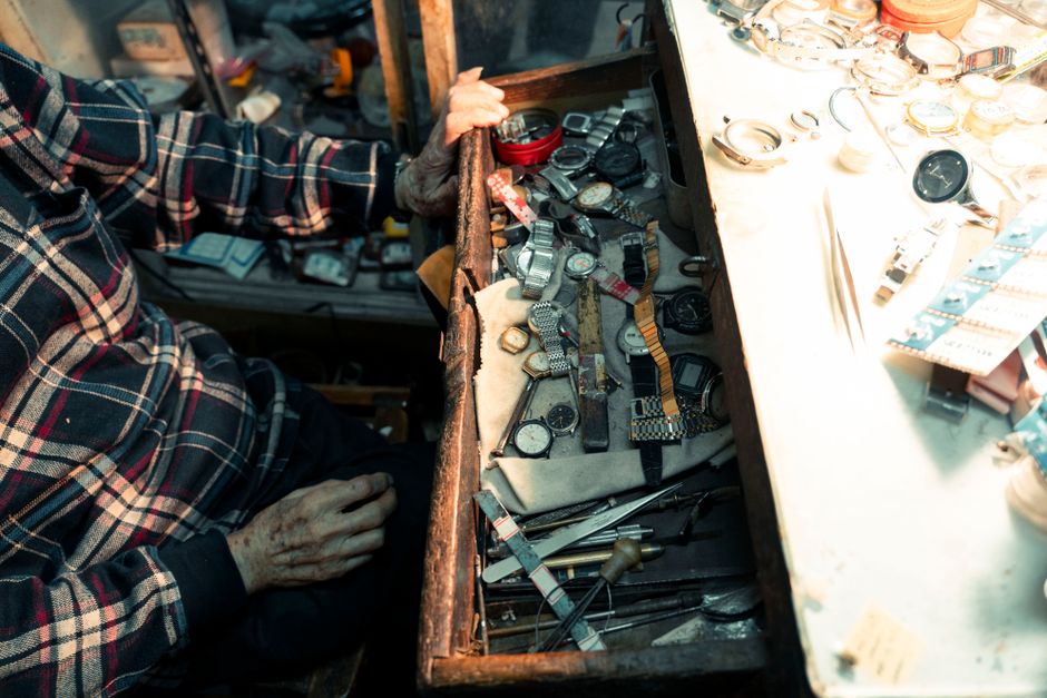 An artisan's hand at a workshop opens a drawer filled with watches, showcasing detailed re