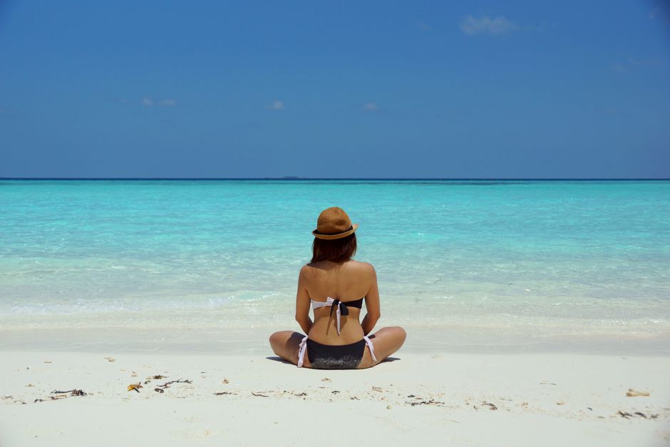 Rear view of a woman in a bikini and hat relaxing on a pristine beach in Maldives.