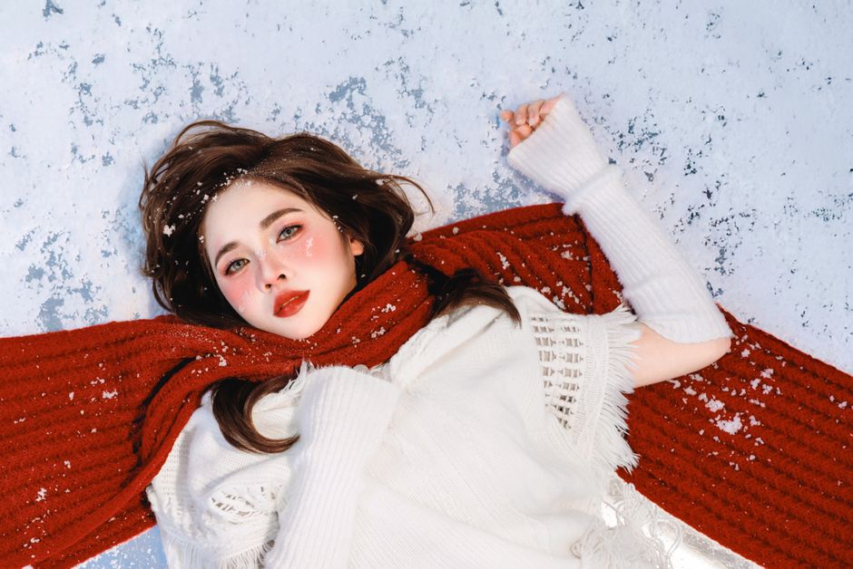 Beautiful winter portrait of a woman lying on the snow in a red scarf.