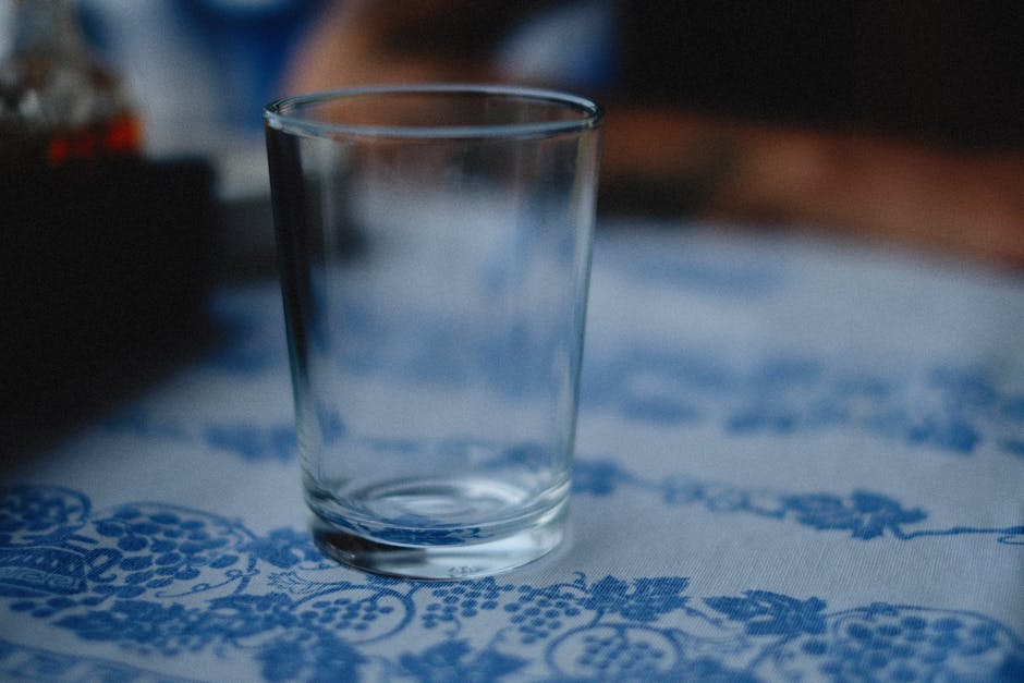 Close-up of an empty drinking glass on a floral-patterned tablecloth with blurred background.