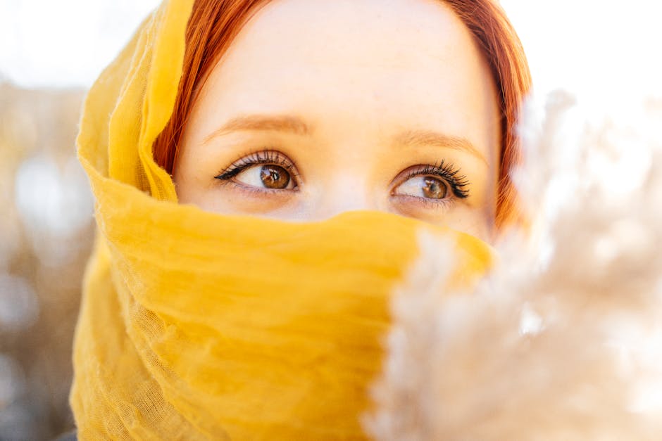 Close-up portrait of a redhead woman with vibrant eyes covered by a yellow scarf.
