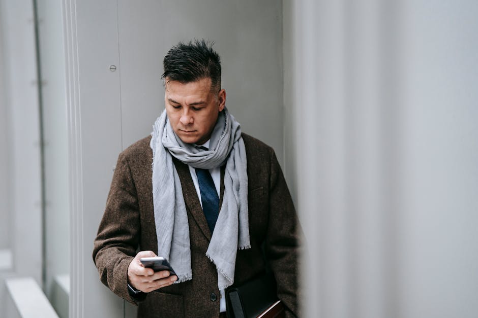 Professional man in a stylish coat and scarf using a smartphone outdoors, representing modern connectivity.