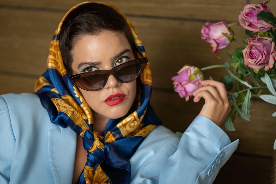 Elegant portrait of a woman in a blue outfit and sunglasses, holding roses, exuding glamour and fashion.