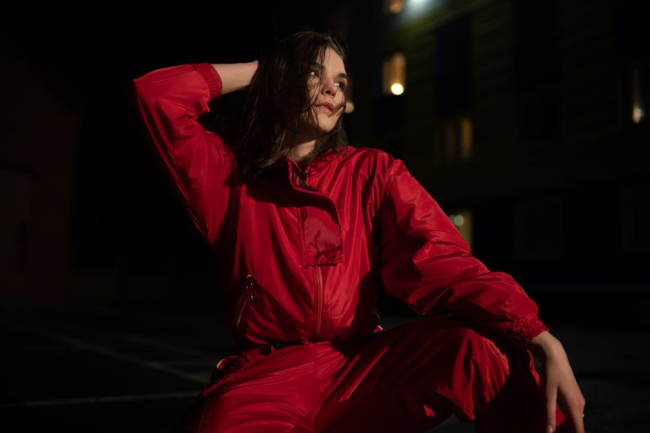 Woman wearing a red jumpsuit posing outdoors at night with dramatic lighting.