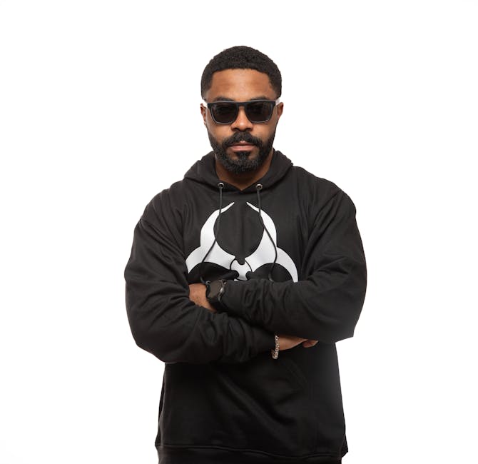 Confident man in a black printed hoodie with sunglasses in studio setting.