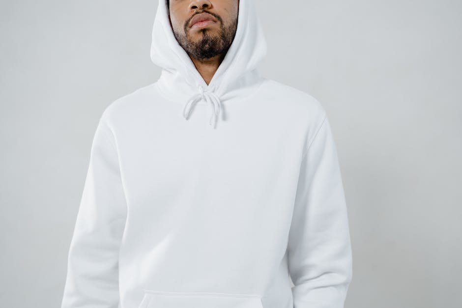 A close-up portrait featuring a man wearing a white hoodie against a light backdrop.