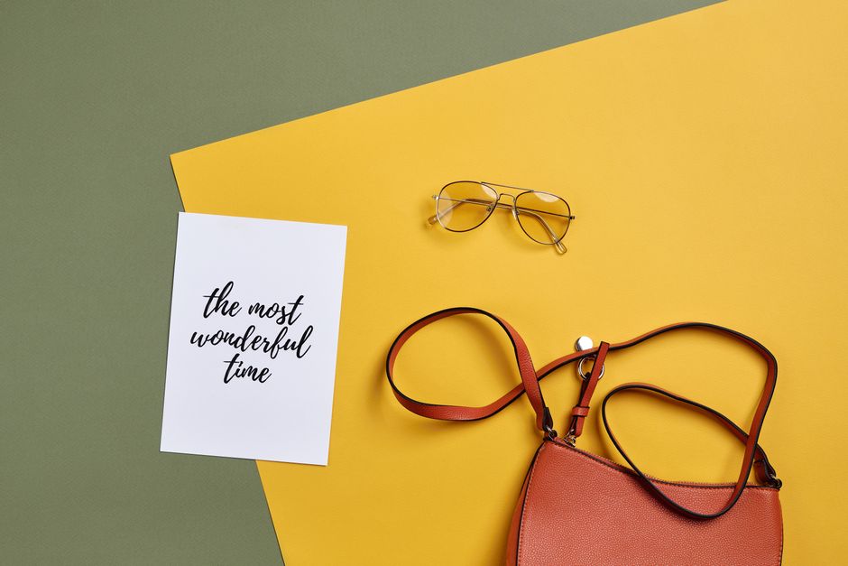 Flat lay featuring a handbag, sunglasses, and inspirational card on colorful background.