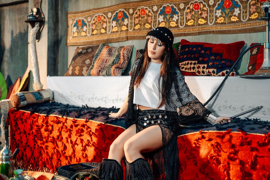 Elegant woman in bohemian attire sitting gracefully in a richly decorated room.