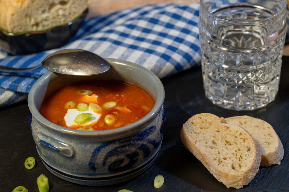 Bowl of hearty solyanka soup with sour cream, garnished with green onions, served with bre