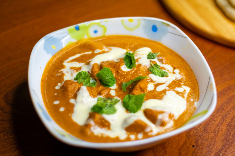 Close-up of a butter chicken curry garnished with cream and mint leaves, served in a bowl.
