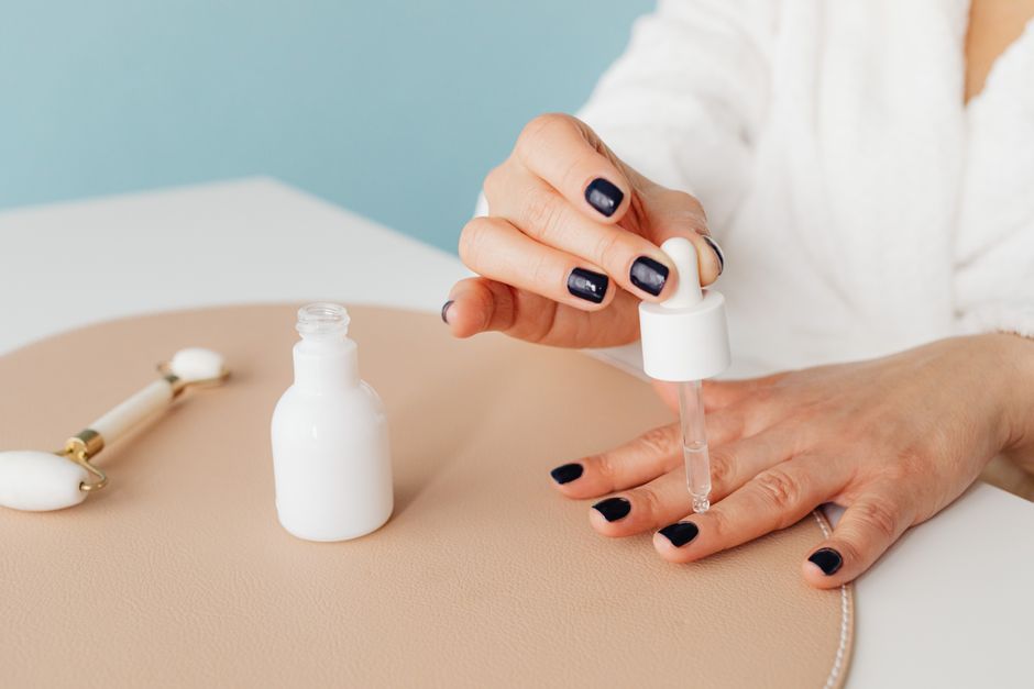 Close-up of a woman applying nail oil with a dropper for manicure care on blue background.
