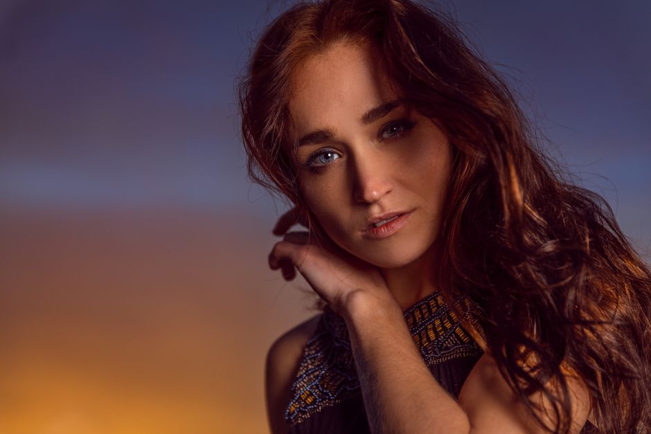 Close-up portrait of a woman with striking blue eyes and long hair at sunset.