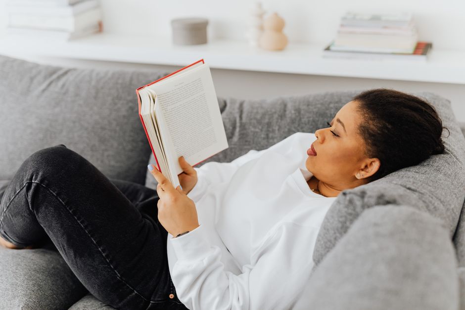 An adult woman enjoys a quiet reading session on a cozy gray couch indoors.
