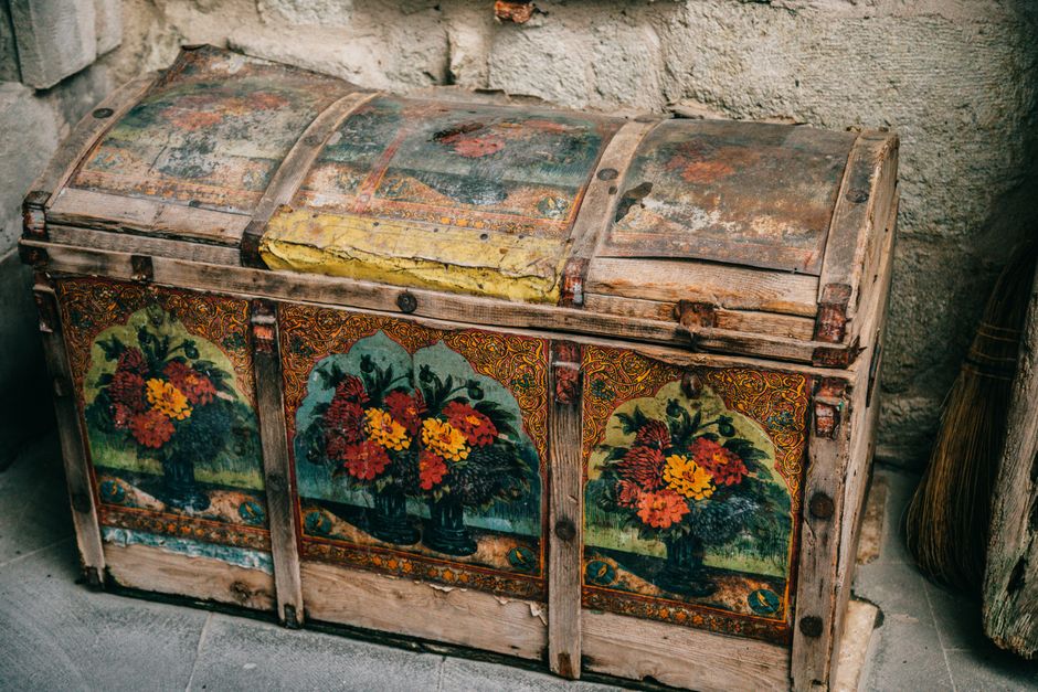 From above of aged shabby wooden box with colorful ornaments and elements placed near stone wall on ground in ancient city