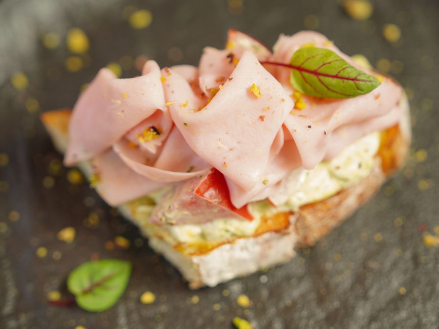 Delicious open-faced sandwich with ham, cream cheese, and fresh toppings on rustic bread.