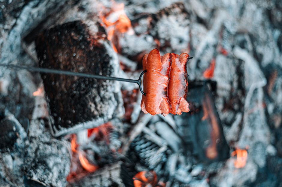 Close-up of sausages grilling on open fire, offering outdoor cooking vibes.