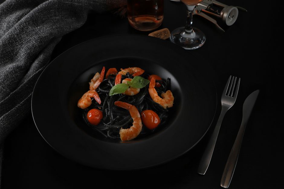 Elegant black pasta dish with shrimp and tomatoes on a dark background.