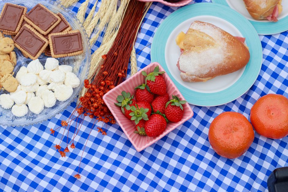 A vibrant picnic setup featuring fresh strawberries, cookies, sandwiches, and oranges on a checkered tablecloth.