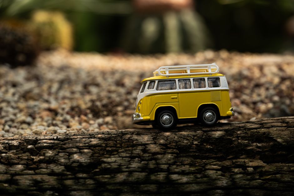 A yellow toy camper on a wooden log, surrounded by natural scenery, depicting travel adventure.