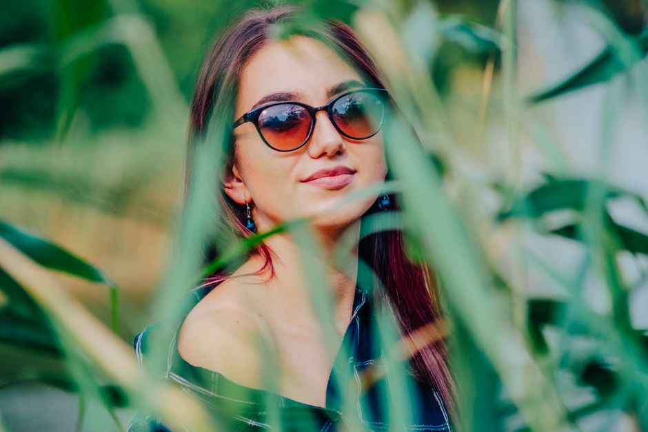 Fashionable woman with sunglasses posing outdoors amidst leaves, exuding style and eleganc