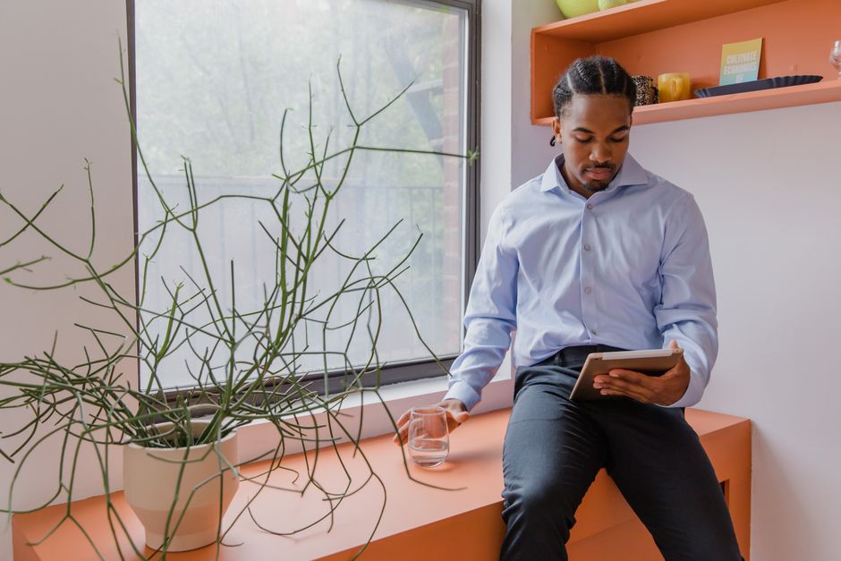 Businessman in casual setting, sitting with a tablet and glass of water indoors by a window.