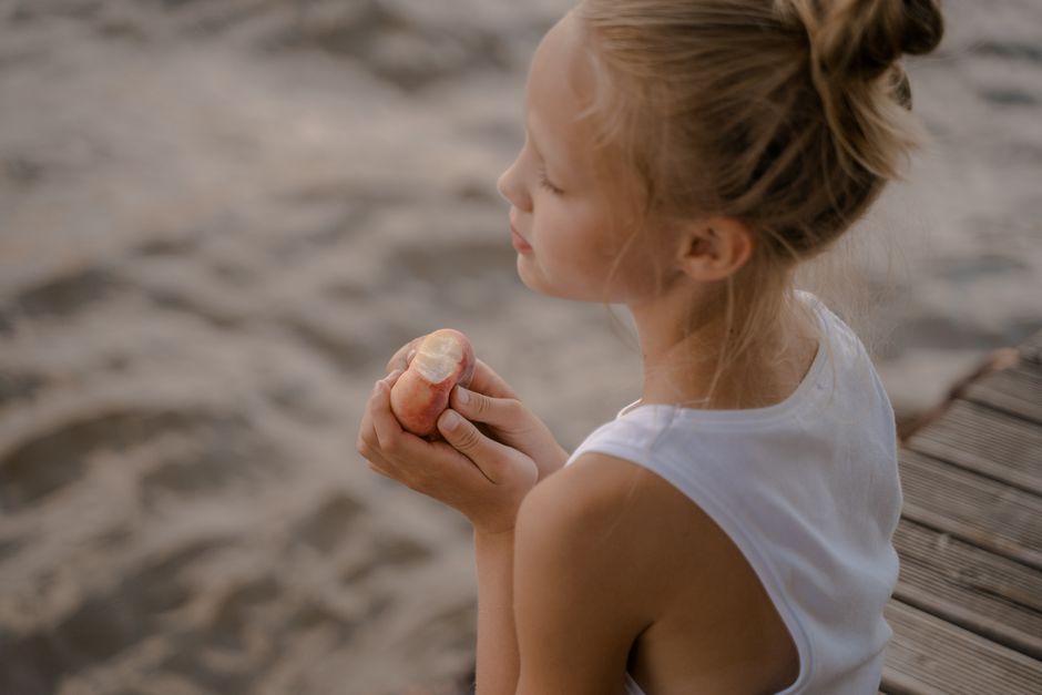 Blond girl enjoying a peach on a pier by the water. Serene summer day.