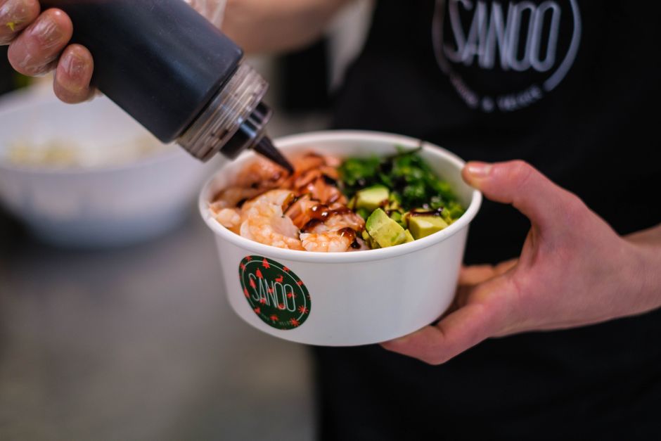 Crop cook in restaurant preparing delicious poke bowl with avocado and shrimps under sauce