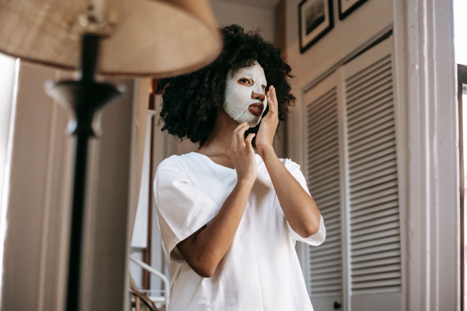 From below of African American female with dark curly hair with sheet mask in casual cloth