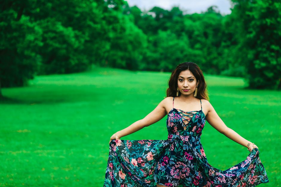 A woman in a floral dress poses gracefully on a lush green lawn in summer.