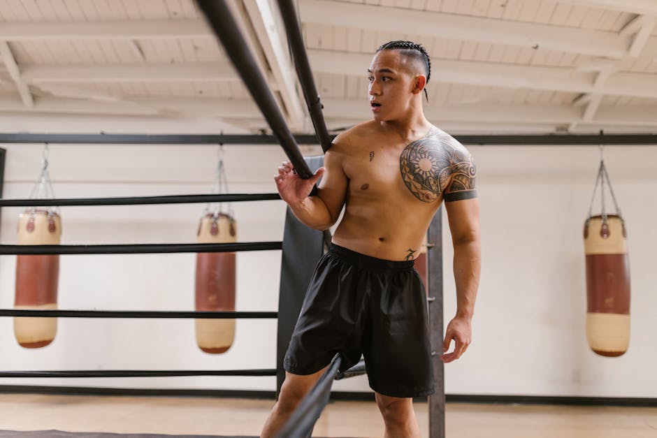 Shirtless martial artist training in a gym with punching bags and a focused expression.