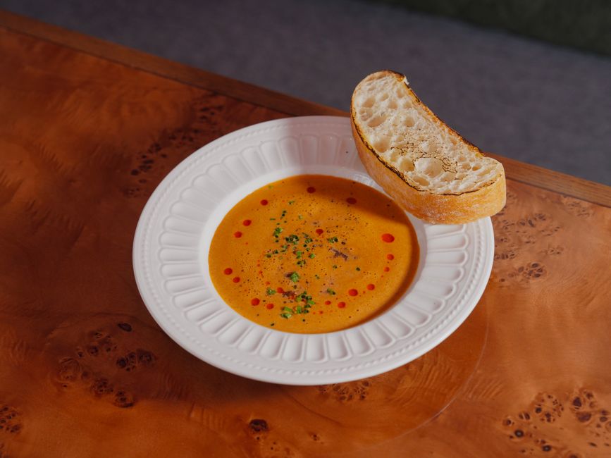 A warm bowl of pumpkin soup garnished with herbs and served with a slice of crusty bread.