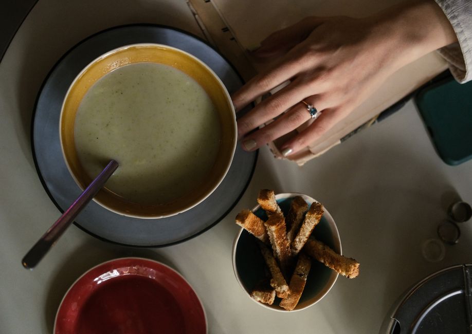 Top view of soup bowl, breadsticks, and hand reaching over a table setting.