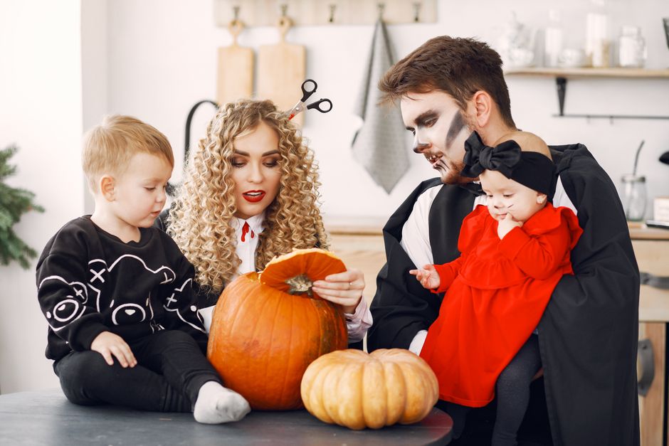 A family dressed in Halloween costumes enjoy carving pumpkins indoors.