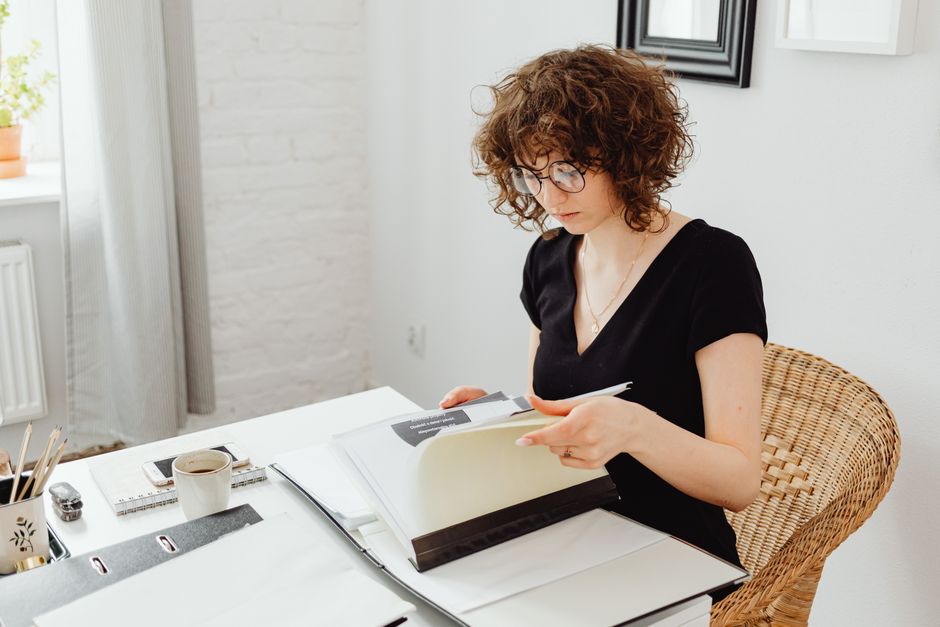 A woman in a black v-neck shirt reading documents while sitting at a desk in an office.