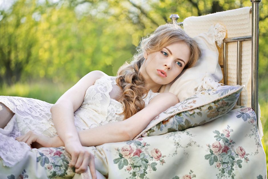 Woman in vintage dress relaxing outdoors with floral bedding during springtime.