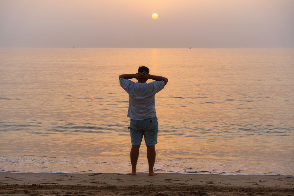 A man stands on Khor Fakkan beach at sunrise, absorbing the serene ocean view.