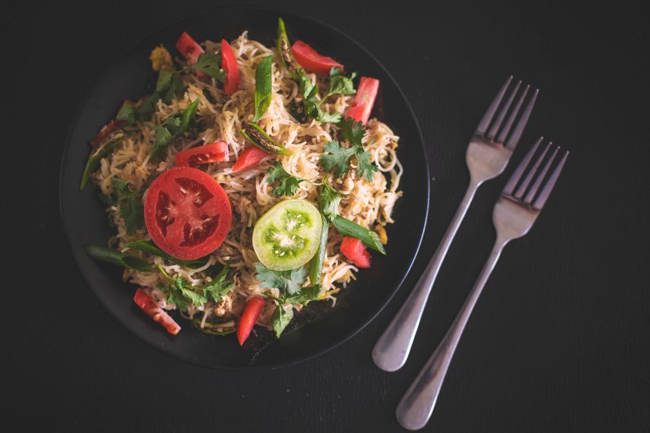 A plate of freshly prepared mixed vegetable noodles garnished with sliced tomatoes and greens.