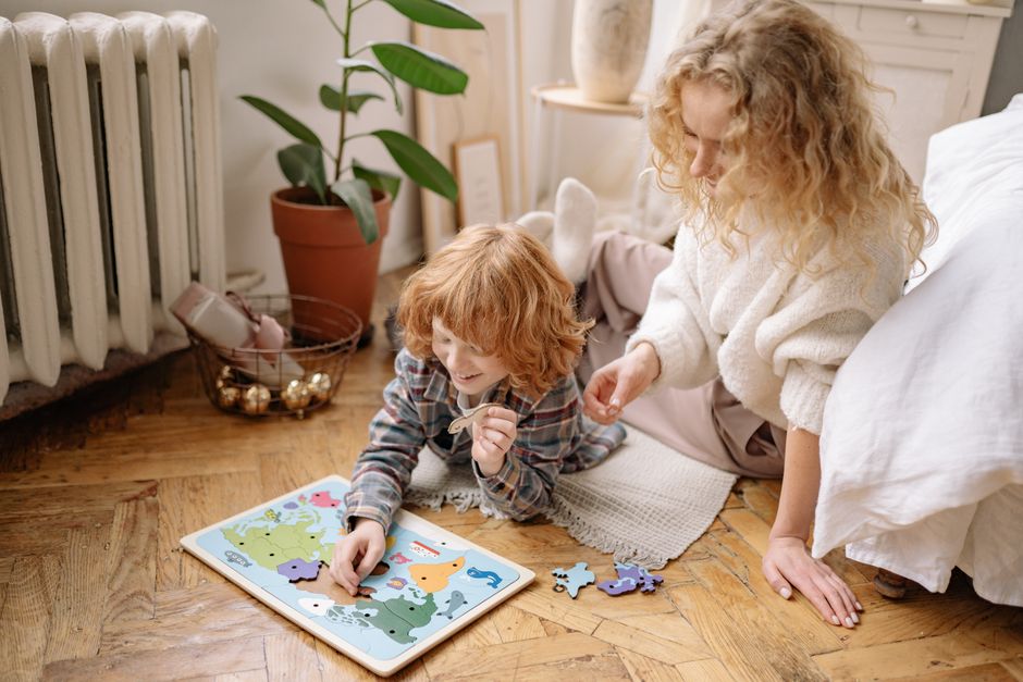A mother and child enjoy a puzzle together on the floor in a cozy indoor setting.