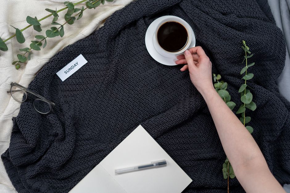 Relaxing Sunday morning setup with coffee, notebook, and glasses on a blanket.