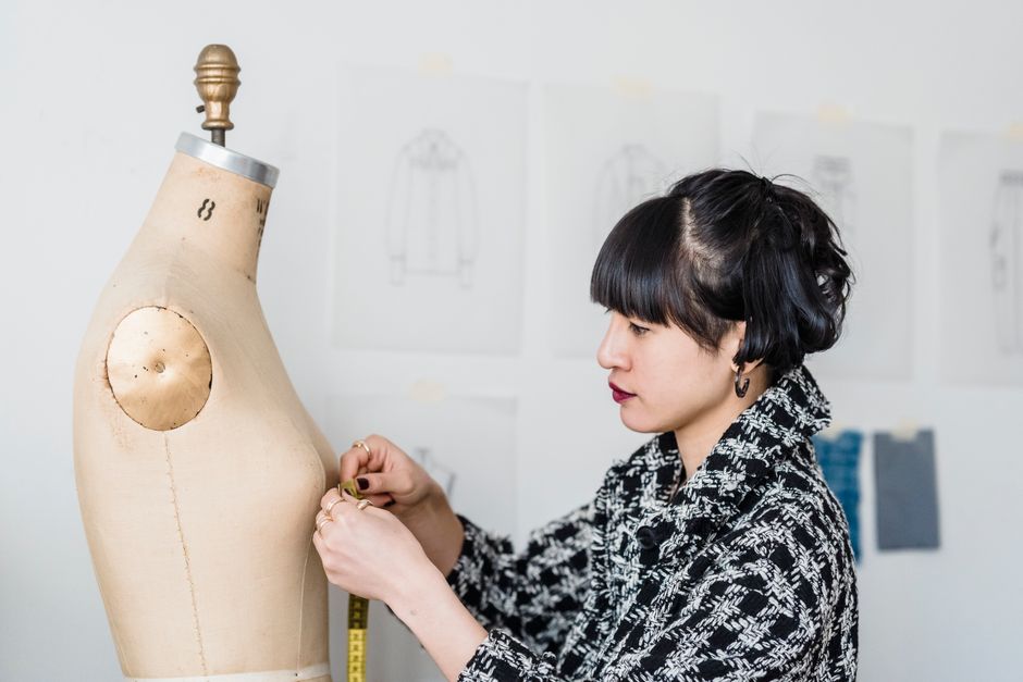 Fashion designer working meticulously on a dress mannequin in a studio setting.